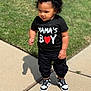 toddler, child, curly_hair, black_tshirt, mamas_boy, red_heart, black_pants, sneakers, sidewalk, grass, outdoor, sunny, shadow, standing, casual_clothing, young_child, person, cute, portrait, daytime