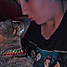 person, cat, tabby_cat, collar, tshirt, graphic_tshirt, animated_characters, face, closeup, indoor, dim_lighting, affection, cute, pet, animal, human, interaction, love, cozy, puckering