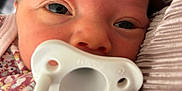 Ellie is registered to the contest to win money with this photo: baby, pacifier, close_up, face, infant, blanket, fabric, pattern, floral, person, skin, head, eyes, mouth, soft_lighting, newborn, cute, resting, portrait, indoors
