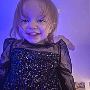 Elyne a rejoint le concours — aidez-le/la à gagner de superbes lots ! black_dress, blue_light, child, clothing, cute, expression, face, hair, happy, indoor, person, portrait, poster, sheer_sleeves, smiling, sparkly, standing, toddler, wall, young_child