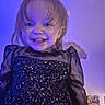Elyne a rejoint le concours — aidez-le/la à gagner de superbes lots ! black_dress, blue_light, child, clothing, cute, expression, face, hair, happy, indoor, person, portrait, poster, sheer_sleeves, smiling, sparkly, standing, toddler, wall, young_child