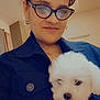 Blanco is registered to the contest to win money with this photo: person, glasses, puppy, dog, white_dog, fluffy, indoor, smile, face, holding, portrait, clothing, jacket, hand, nail_polish, earrings, hair, home, light, warmth