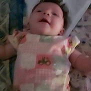 Oaklynn is registered to the contest to win money with this photo: baby, infant, onesie, clothing, lying_down, face, child, smile, bed, bedding, pattern, soft, indoors, cute, happy, skin, person, young, blur, portrait