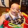 baby, child, infant, smiling, happy, portrait, indoor, activity_center, baby_toys, colorful, playtime, sitting, bib, clothing, cushion, face, hands, toy, furniture, home