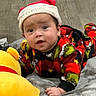 baby, child, infant, santa_hat, holiday, christmas, festive, pajamas, plaid, colorful_clothing, smiling, curious, portrait, indoors, bed, blanket, plush_toy, yellow_toy, wood_floor, sitting