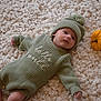 Huxley is registered to the contest to win money with this photo: baby, infant, knitwear, hat, pom_pom, green_clothing, carpet, texture, pumpkins, orange, autumn, cozy, soft, lying_down, cute, child, portrait, indoor, small_pumpkins, festive