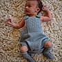 Huxley is registered to the contest to win money with this photo: baby, infant, knitwear, blue_clothing, socks, carpet, soft_texture, lying_down, cute, small, child, cozy, warm, indoors, portrait, newborn, hands, legs, face, curious
