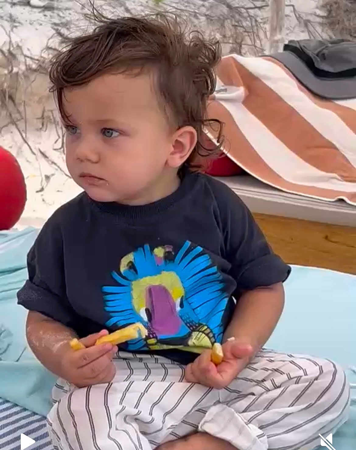 Marcel a rejoint le concours — aidez-le/la à gagner de superbes lots ! toddler, child, fries, blue_eyes, curly_hair, striped_pants, black_tshirt, beach_towel, sand, outdoor, sitting, food, casual_clothing, summer, relaxed, portrait, daytime, snack, serious_expression, barefoot