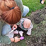 Mercy is registered to the contest to win money with this photo: toddler, adult, grass, wood_chips, outdoor, toy, sitting, green_sweater, jeans, pink_shoes, scarf, hair_clip, playing, ground, nature, person, child, footwear, casual_clothing, daylight