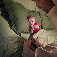 Mercy joined the competition — help win amazing prizes! baby, bed, pillow, blanket, person, hands, wooden_headboard, green_bedding, indoor, child, sleepwear, curious, cozy, portrait, infant, looking, human, comfort, rest, candid