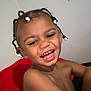 child, smiling, laughing, braids, beads, happy, face, skin, red_cushion, indoor, young, person, hair, cute, teeth, joy, bare_shoulders, expression, portrait, fun