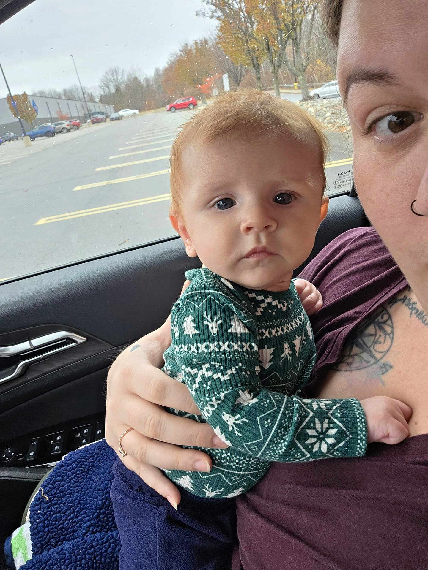 Atlas is registered to the contest to win money with this photo: baby, child, person, adult, car_interior, window, parking_lot, autumn, trees, tattoo, nose_ring, hand, clothing, sweater, green, blue_blanket, expression, face, holding, indoor