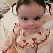 Ariel Rae joined the competition — help win amazing prizes! baby, child, pigtails, face, eyes, smile, cute, indoor, clothing, heart_pattern, ruffles, person, skin, hair, infant, sitting, portrait, closeup, home, adorable