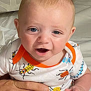 Braxton is registered to the contest to win money with this photo: baby, infant, child, smile, onesie, clothing, hand, person, cute, happy, indoor, bed, fabric, skin, head, face, blue_eyes, short_hair, young, holding