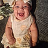 baby, smiling, headband, dress, infant, happy, person, indoors, couch, hand, texture, clothing, cute, child, portrait, seated, human, expression, baby_girl, comfort