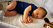 Hudson is registered to the contest to win money with this photo: baby, sleeping, crib, onesie, socks, plush_toy, pacifier, star_pattern, nursery, infant, resting, child, cute, soft_lighting, indoors, bed, peaceful, face, hand, foot