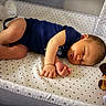 baby, sleeping, crib, onesie, socks, plush_toy, pacifier, star_pattern, nursery, infant, resting, child, cute, soft_lighting, indoors, bed, peaceful, face, hand, foot