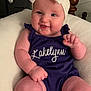 baby, child, smile, headband, bow, purple_outfit, cushion, indoor, arm, leg, face, person, cute, happy, infant, plump, seated, furniture, skin, portrait