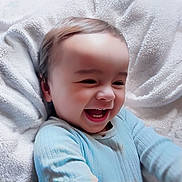 Mateo is registered to the contest to win money with this photo: baby, child, laughing, smiling, onesie, blue_clothing, blanket, soft_texture, happy, infant, cute, portrait, face, head, cheerful, young_child, closeup, indoor, skin, person