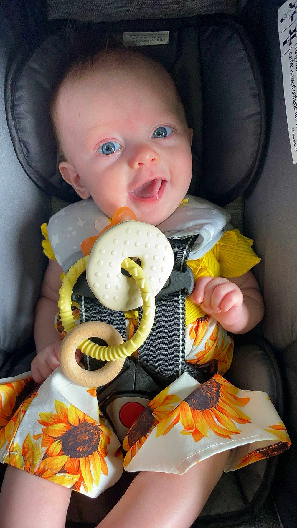 Olivia joined the competition — help win amazing prizes! baby, child, smiling, car_seat, blue_eyes, sunflower_pattern, yellow_clothing, teething_toy, infant, cute, happy, seat_belt, fabric, indoor, closeup, young_child, playful, comfort, portrait, person