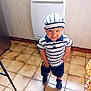 Maylone participe au concours pour gagner de l'argent avec cette photo : child, boy, striped_hat, striped_shirt, shorts, sandals, indoor, tiled_floor, playful, smile, hands_on_hips, wall_paneling, appliance, kitchen, young_child, footwear, hat, clothing, person, portrait