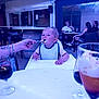 toddler, child, feeding, high_chair, bib, spoon, food, outdoor, restaurant, table, glass, adult, people, conversation, casual, seated, drink, beverage, dining, family
