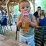 Maylone a rejoint le concours — aidez-le/la à gagner de superbes lots ! toddler, child, water_bottle, indoor, wooden_structure, table, chair, people, casual_clothing, greenery, backpack, restaurant, curious, drink, person, hairstyle, summer, daylight, relaxed, dining