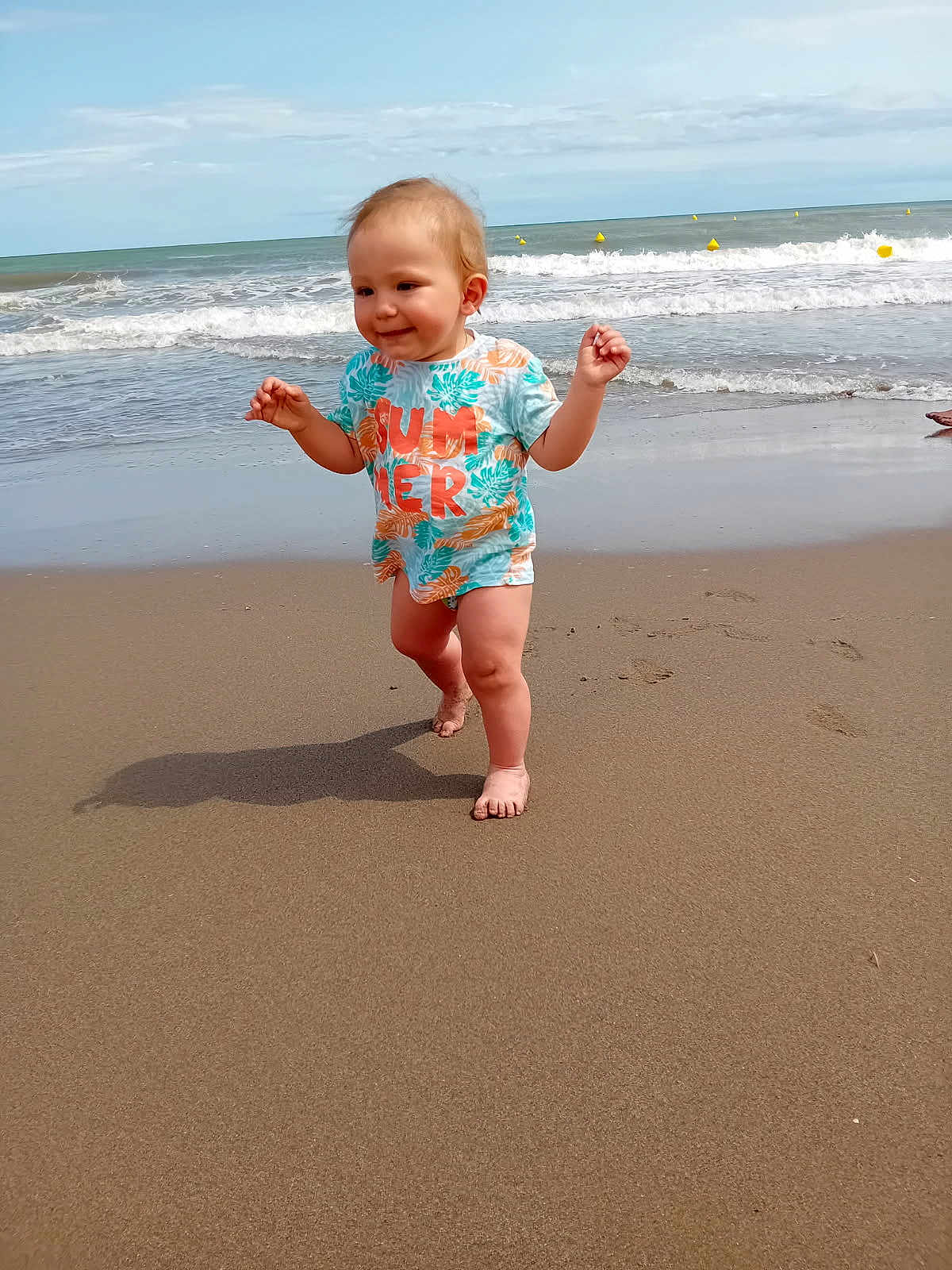 Maylone a rejoint le concours — aidez-le/la à gagner de superbes lots ! toddler, child, beach, sand, ocean, waves, sky, shirt, summer, barefoot, walking, happy, water, coast, outdoor, nature, playful, person, daytime, shore