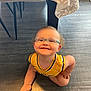 toddler, child, glasses, yellow_jersey, lakers, floor, table, tablecloth, smile, happy, indoor, crawling, person, baby, cute, curly_hair, barefoot, wooden_floor, furniture, bright