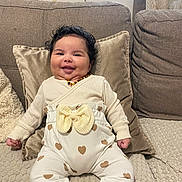 Dahyssa participe au concours pour gagner de l'argent avec cette photo : amber_necklace, baby, blanket, bow, chubby_cheeks, couch, cozy, curtain, cute, happy, heart_pattern, infant, living_room, onesie, pillow, portrait, sitting, smiling, soft_texture, upholstery