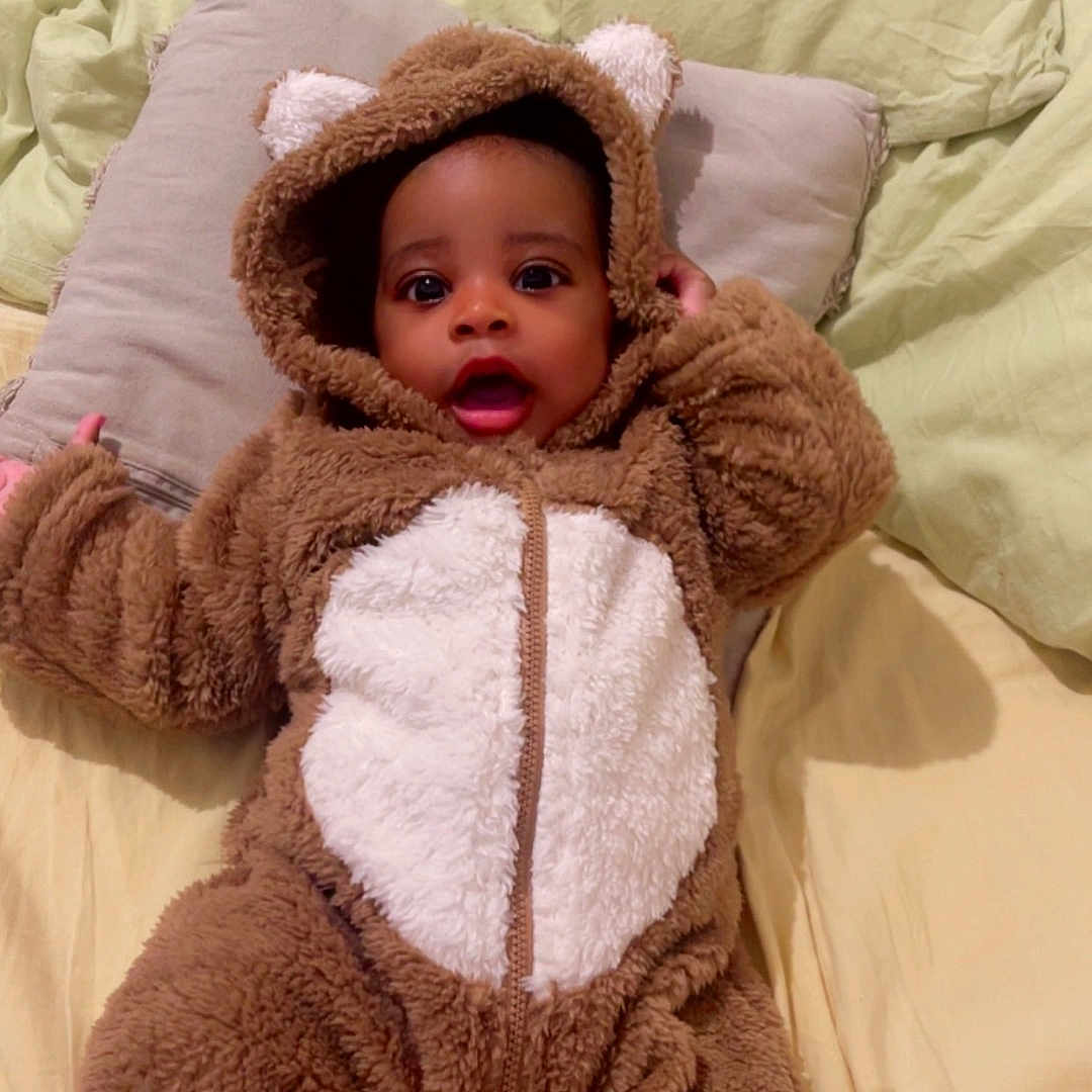 Jaïs participe au concours pour gagner de l'argent avec cette photo : baby, bear_suit, bed, blanket, child, costume, cute, eyes, face, fur, hooded, indoors, infant, mouth, person, pillow, sleepwear, smiling, soft, warm