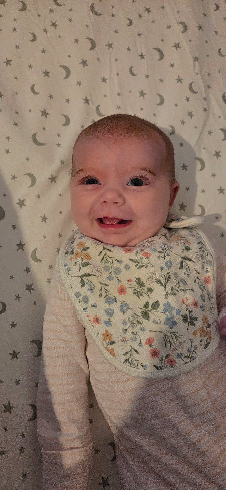 baby, bib, blanket, child, clothing, cute, face, floral, happy, infant, lying_down, moon, onesie, patterned, portrait, skin, sleepwear, smiling, stars, young