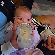 Hope is registered to the contest to win money with this photo: baby, bottle, feeding, hand, person, clothing, indoor, purple_outfit, infant, adult, holding, face, eyes, sleeve, cradle, baby_bottle, feeding_time, close_up, resting, nursery