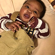 Javen joined the competition — help win amazing prizes! baby, beige_background, child, clothing, cute, face, hands, happy, indoors, infant, laying_down, maroon, overalls, person, playful, portrait, smiling, soft_light, striped_shirt, young_child