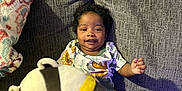 Nora is registered to the contest to win money with this photo: baby, child, couch, plush_toy, stuffed_animal, blanket, smiling, indoor, person, clothing, soft_toy, seated, home, furniture, cute, happy, curly_hair, colorful, cozy, portrait
