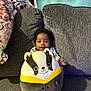 Nora is registered to the contest to win money with this photo: baby, plush_toy, couch, blanket, smiling, indoor, child, person, soft_toy, cute, happy, seated, fabric, cozy, home, colorful, comfortable, young_child, portrait, relaxing