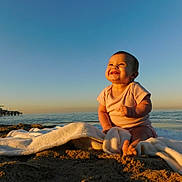 Isla is registered to the contest to win money with this photo: baby, infant, beach, ocean, pier, sunset, towel, sand, smiling, joy, sunlight, sky, horizon, seascape, barefoot, portrait, outdoor, cloudless, cute, summer