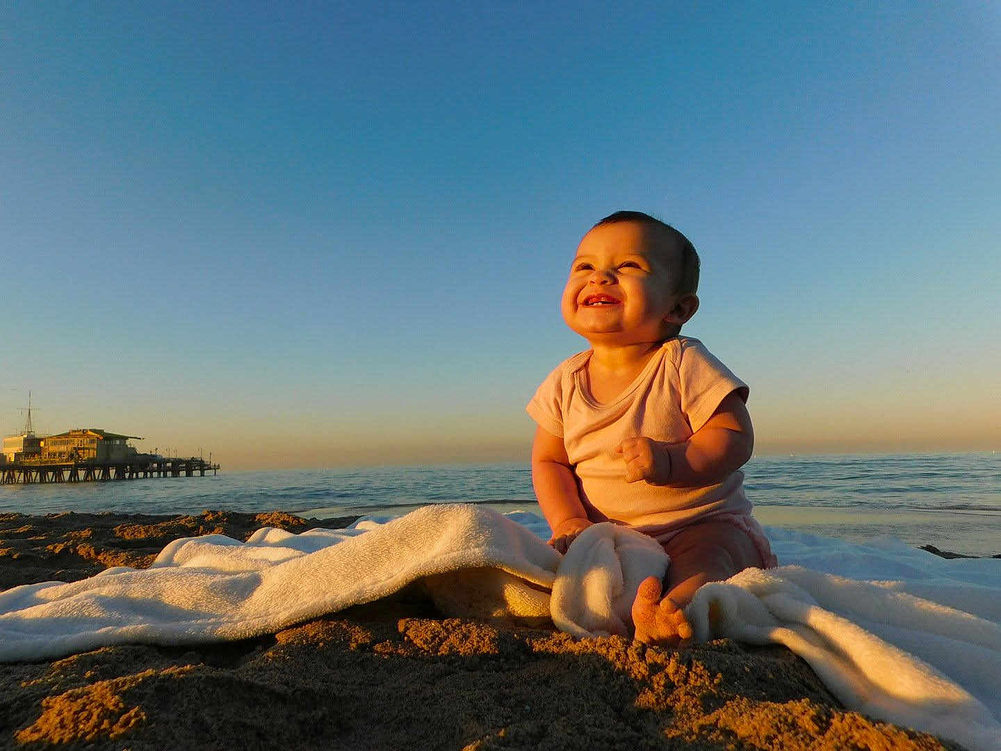 Isla is registered to the contest to win money with this photo: baby, infant, beach, ocean, pier, sunset, towel, sand, smiling, joy, sunlight, sky, horizon, seascape, barefoot, portrait, outdoor, cloudless, cute, summer