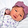 newborn, baby, blanket, purple_bow, headband, face, skin, hand, wrapped, sleeping_area, soft_texture, closeup, cute, infant, portrait, resting, cozy, babywear, fabric, bed