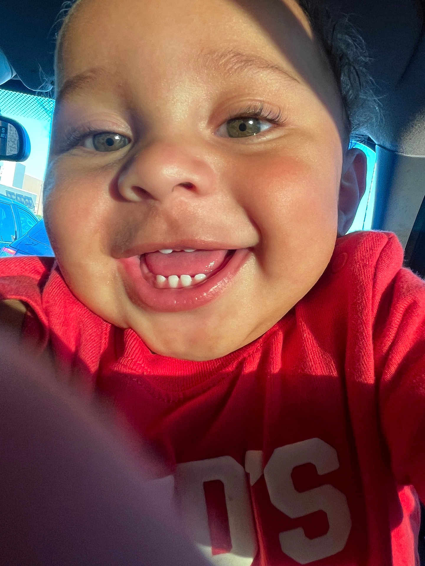 Kane is registered to the contest to win money with this photo: toddler, child, smile, face, closeup, red_shirt, teeth, joyful, indoors, car_interior, sunlight, eyes, nose, mouth, person, happy, portrait, casual, cute, expression