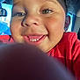 child, toddler, smile, face, eyes, finger, selfie, car, window, sunlight, happy, closeup, red_clothing, skin, cheeks, teeth, hair, interior, daylight, vehicle