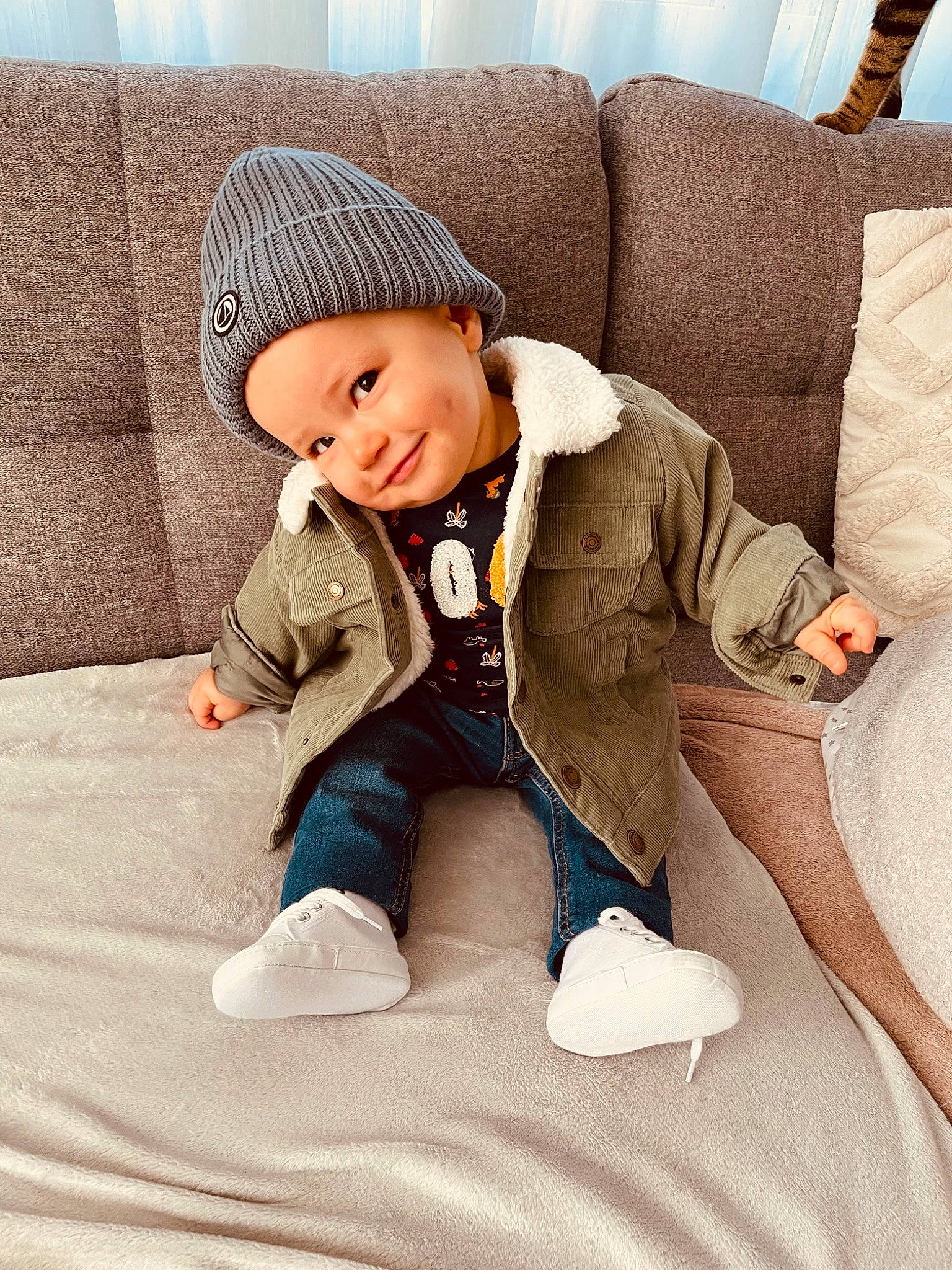 Ezra participe au concours pour gagner de l'argent avec cette photo : baby, baby_toddler_clothing, cap, child, comfort, couch, facial_expression, fashion_accessory, flooring, foot, happy, headwear, joy, leg, linens, outerwear, person, sitting, skin, sleeve