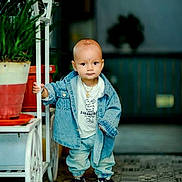 Jarvis is registered to the contest to win money with this photo: toddler, child, denim_jacket, sneakers, indoor, potted_plant, cart, floor_tiles, curious, standing, casual_clothing, portrait, young_child, cute, fashionable, jewelry, baby, person, floor, background_blur