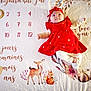 baby, red_dress, headband, blanket, numbers, text, french_text, deer, squirrel, flower, pattern, infant, cute, lying_down, soft_texture, child, smiling, illustration, woodland_animals, warm_colors