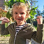 child, smiling, leaf_crown, outdoor, sunny, curly_hair, jacket, greenery, playful, young, happy, nature, tree, blue_sky, portrait, person, casual_clothing, daylight, face, boy