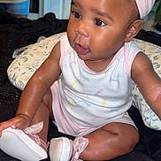 Whyinter Young is registered to the contest to win money with this photo: baby, child, infant, headband, bow, sitting, indoors, clothing, shoes, pillow, bedspread, curly_hair, cute, skin, face, person, young_child, looking_away, pink, white
