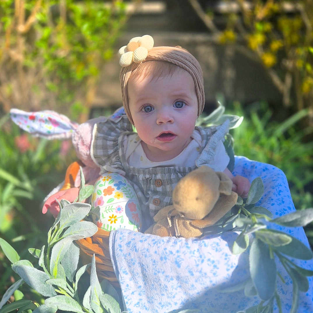 Leighton is registered to the contest to win money with this photo: baby, basket, blanket, child, clothing, curious, cute, easter_egg, face, flower, garden, greenery, headband, infant, nature, outdoor, plush_toy, portrait, soft_light, spring