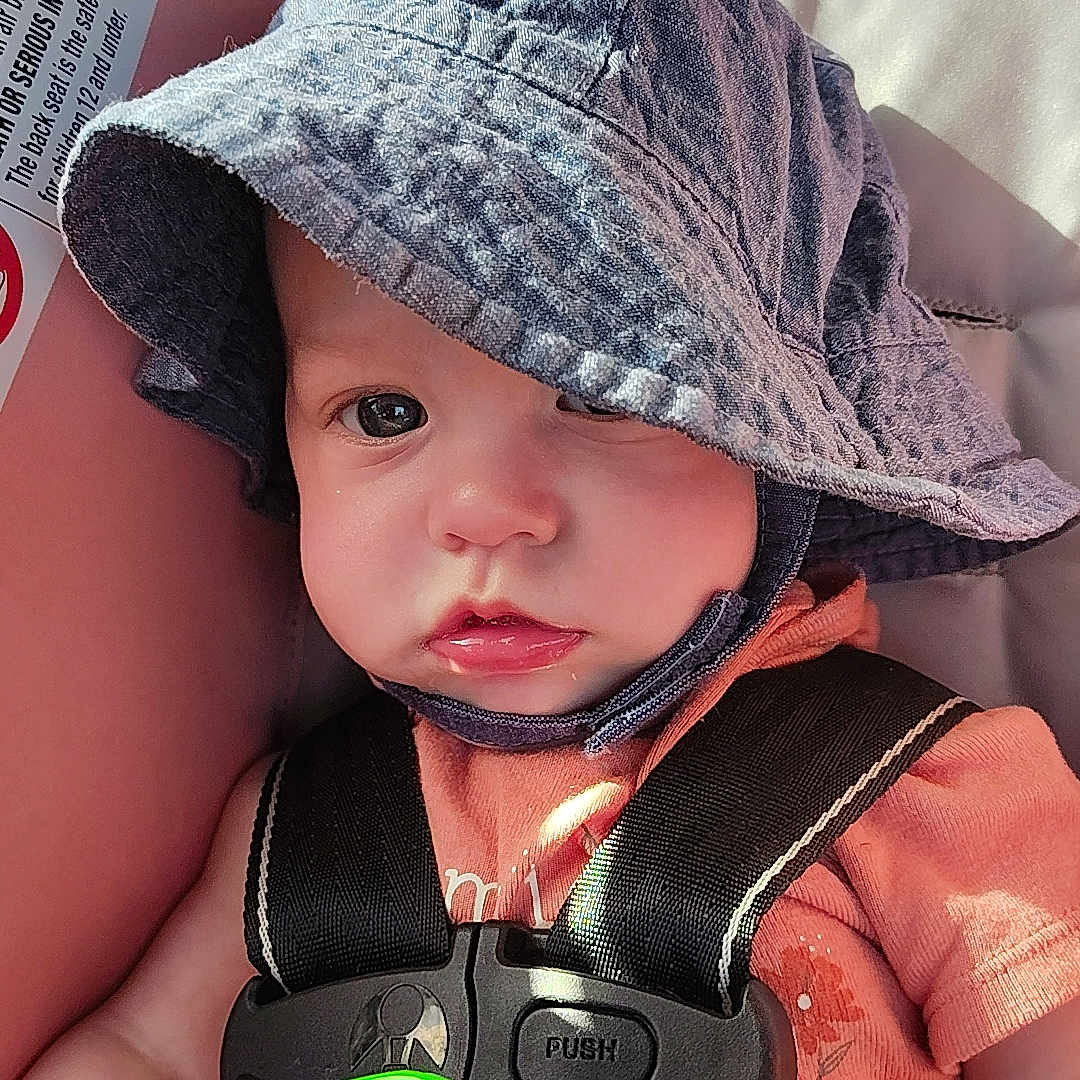 Willow joined the competition — help win amazing prizes! baby, bucket_hat, car_seat, child, closeup, clothing, cute, expression, face, hand, hat, indoors, infant, light, portrait, rattle, safety, seatbelt, skin, toy