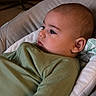 baby, child, infant, green_clothing, ribbed_fabric, cushion, seat, indoors, musical_instrument, banjo, face, head, ear, expression, comfort, relaxation, portrait, side_view, soft_lighting, homely