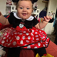 Rayne is registered to the contest to win money with this photo: baby, child, costume, minnie_mouse, dress, polka_dots, headband, smile, blue_eyes, curly_hair, indoors, chair, clothing, person, cute, happy, sitting, toy, footwear, playful